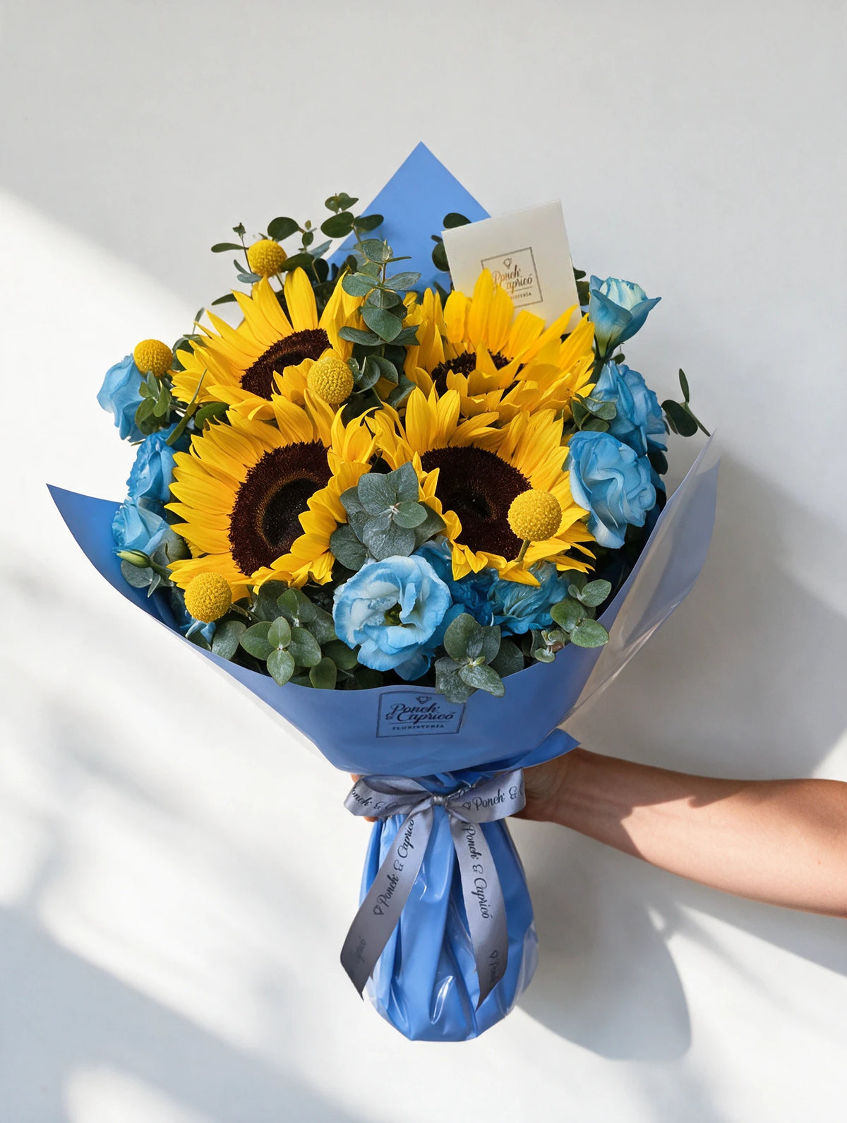 Ramo de Girasoles, Lisianthus tintado a mano en azul, Craspedia y Dólar en envoltura azul - Ponch & Caprico PRAM066