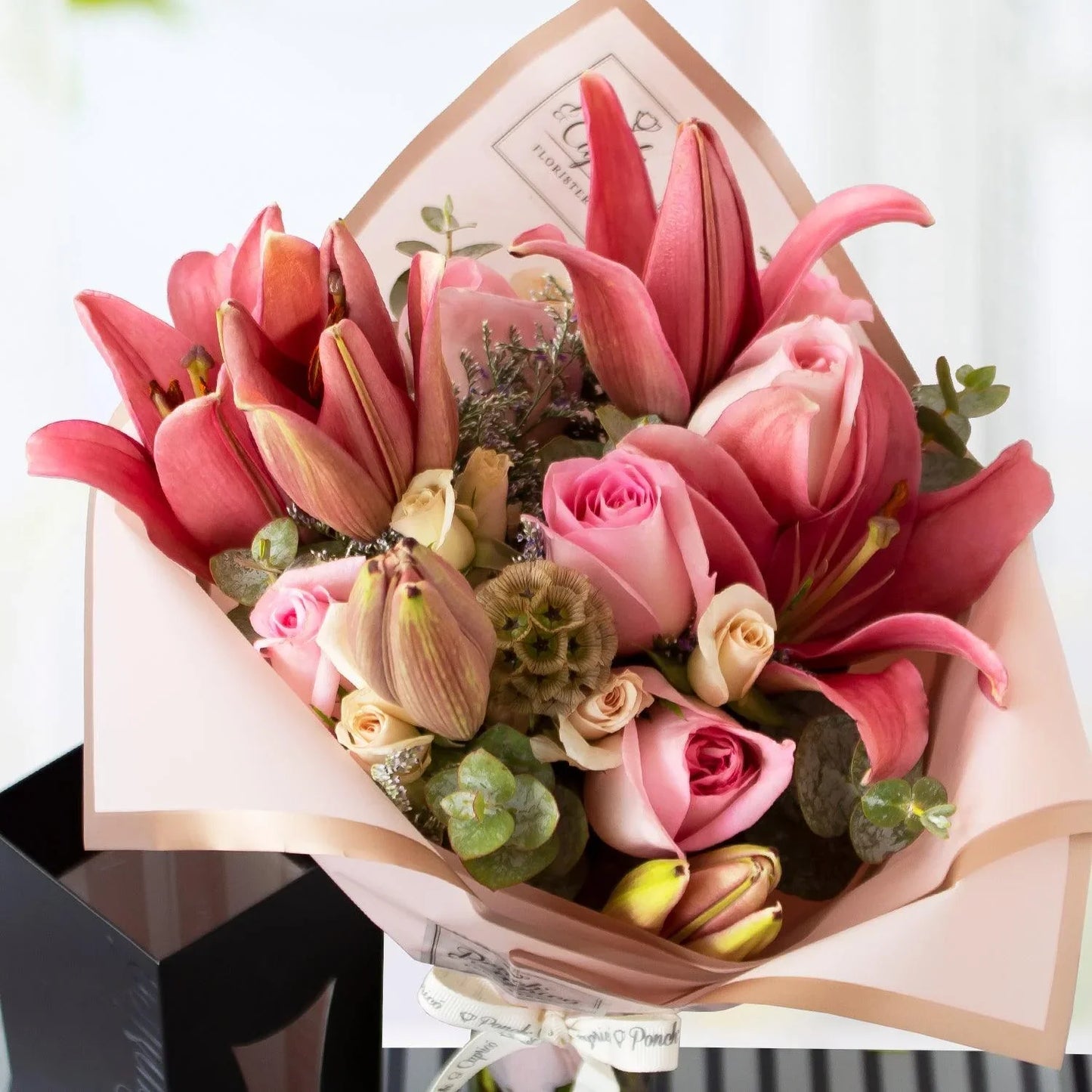 Lindo ramillete atado a mano de Rosas, Lillies, Mini Rosas y Escabiosa, Limonio y follaje; envuelto en elegante papel y delicado moño pequeño de tela.