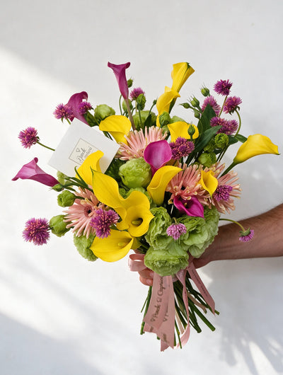 Ramo de flores con calas de agua amarillas y fucsia, gerbera rosa, lisianthus verde y allium en florero - Ponch & Caprico ALA033