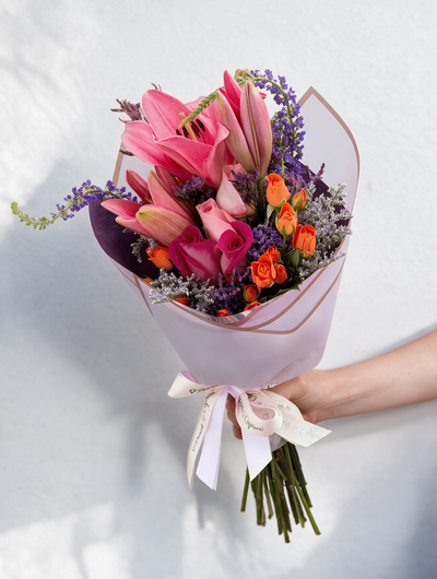 Lindo ramillete atado a mano de Mini Rosas Naranja, Lillies, Rosas Rosada, Rosas Fucsia, Espuma, Verónica y Limonio, envuelto en finos papeles y delicado moño de tela.  Viene incluido florero de vidrio, y caja que cubre el florero (esta última únicamente en la presentación sencilla).