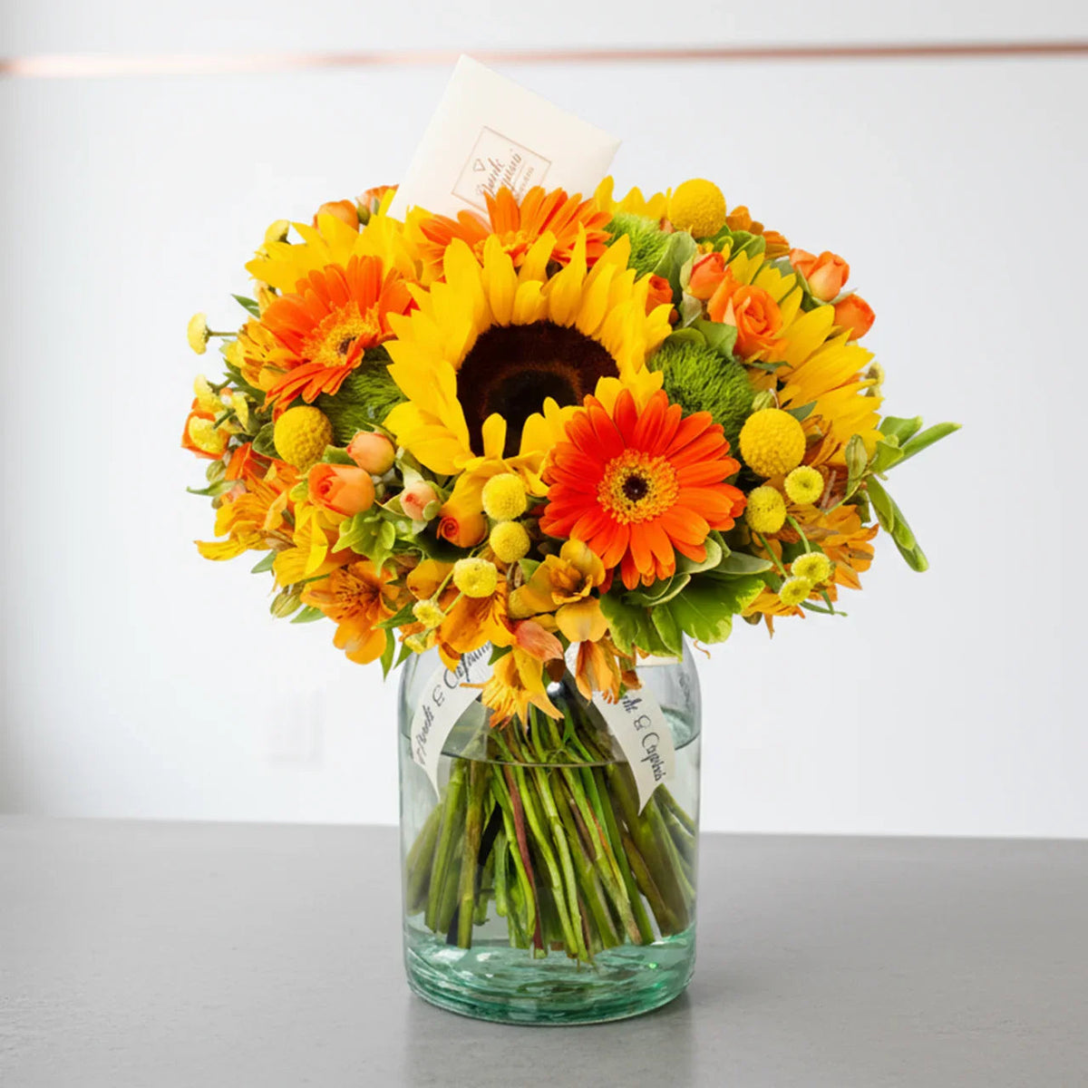 Ramo de gerberas y girasoles con mini rosas naranja en florero de vidrio — componente del set