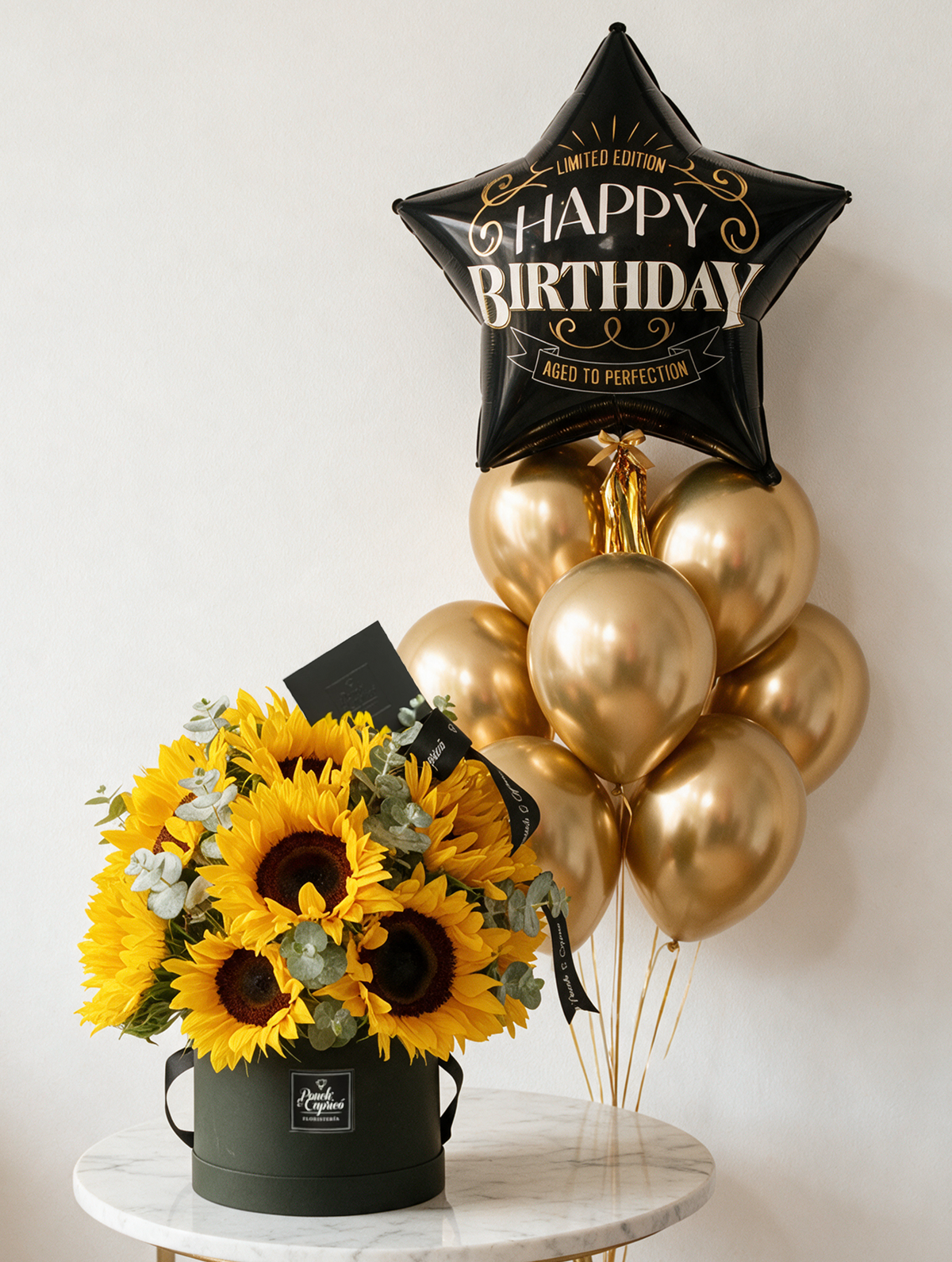 Set de regalo: domo de girasoles frescos junto a bouquet de globos con estrella negra Better With Age y ocho globos cromo dorado con helio