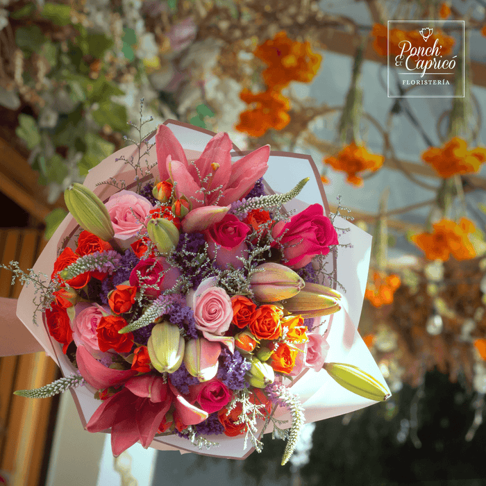 Lindo ramillete atado a mano de Mini Rosas Naranja, Lillies, Rosas Rosada, Rosas Fucsia, Espuma, Verónica y Limonio, envuelto en finos papeles y delicado moño de tela.  Viene incluido florero de vidrio, y caja que cubre el florero (esta última únicamente en la presentación sencilla).